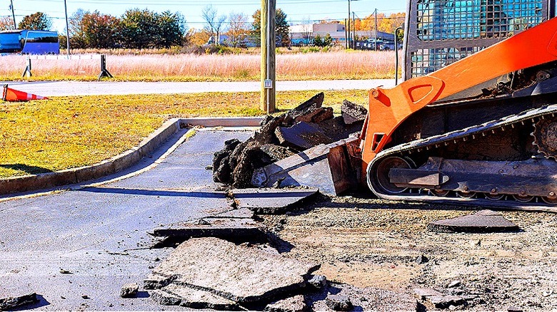 Skid steer tears up the asphalt of an empty parking lot