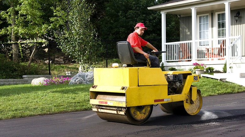 A person smoothing out a home asphalt driveway with a roller