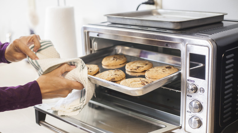 person removing metal pan with cookies from toaster oven