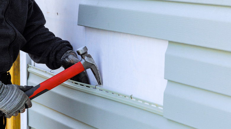 A person in a black coat and wearing gray-and-black striped gloves uses a hammer to replace peeling vinyl planks