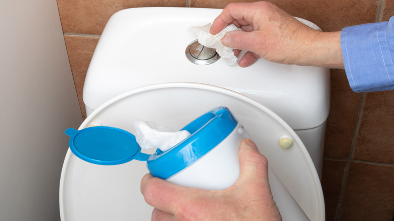 Hand using disinfectant wipe to clean push button of toilet