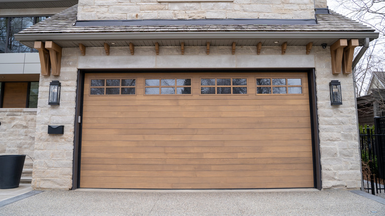 A view of a closed wooden garage door from a brick house.