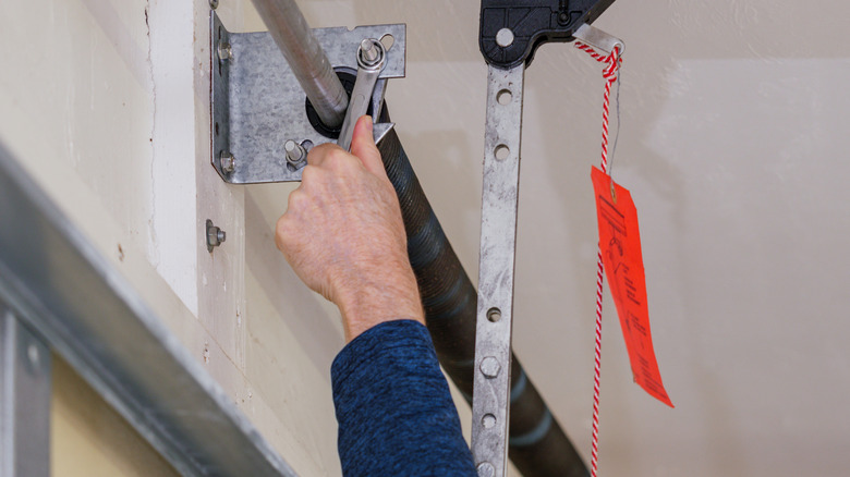 A socket wrench being used on an electric garage door's coiled tension spring.