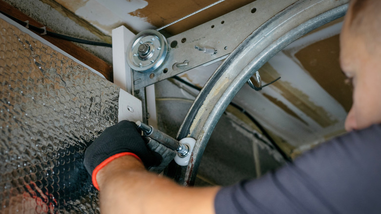 A person repairing a garage door'd track rollers inside.