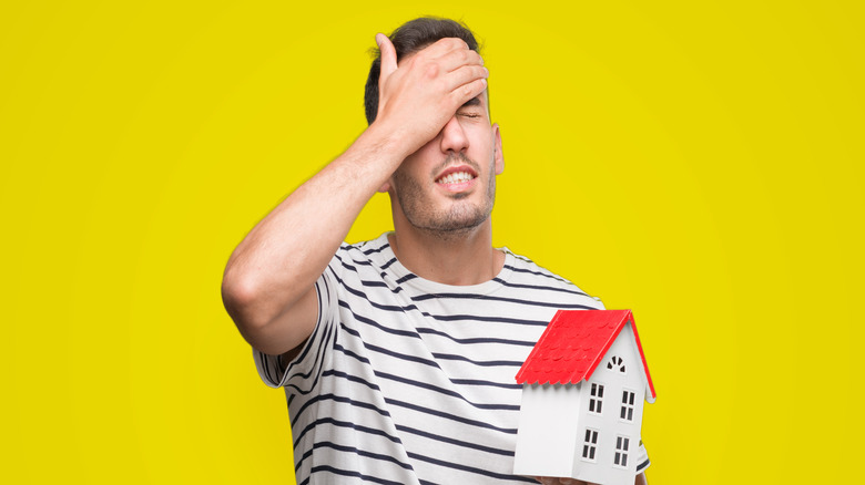 Frustrated man holding house miniature