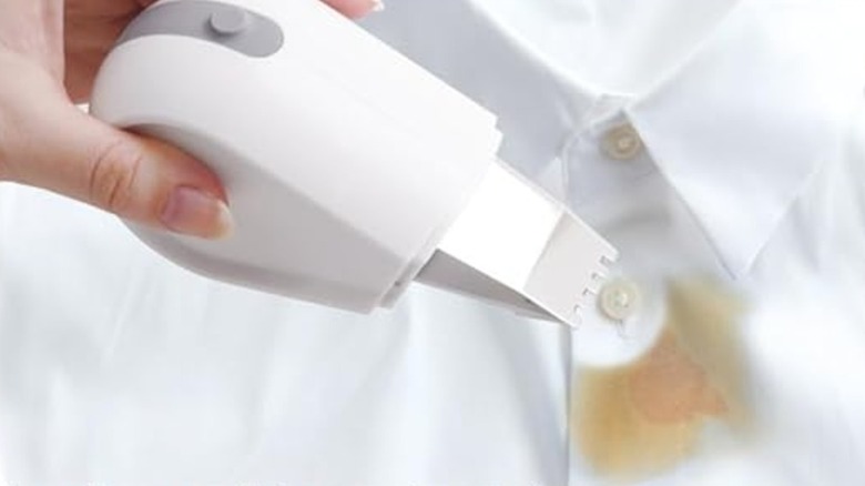 Female hand holding a small stain remover over a stained white shirt