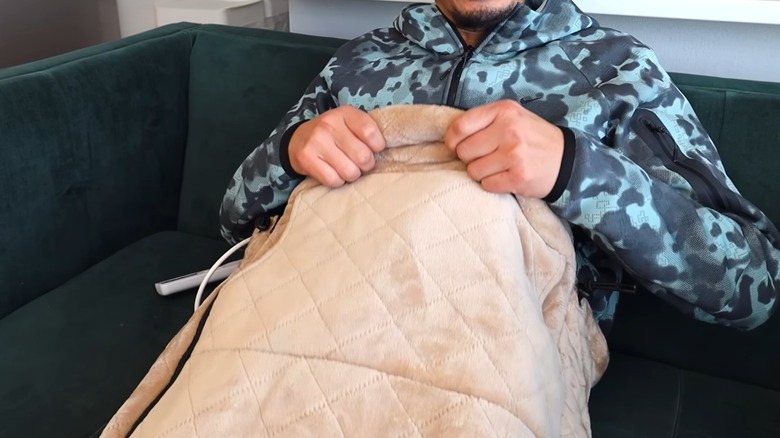 Man pulling up a wearable heated blanket with the remote lying nearby