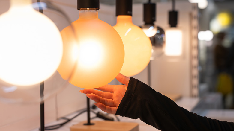 A person touching a large exposed bulb lamp