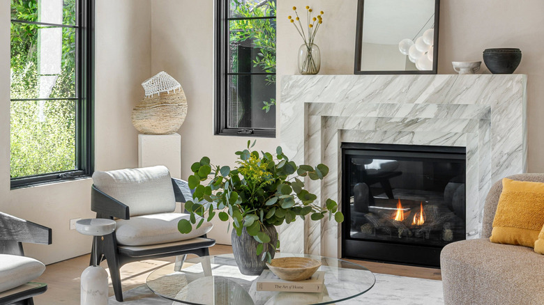 Elegant living room with marble fireplace, vases on the mantel, and glass coffee table surrounded by chairs and a sofa