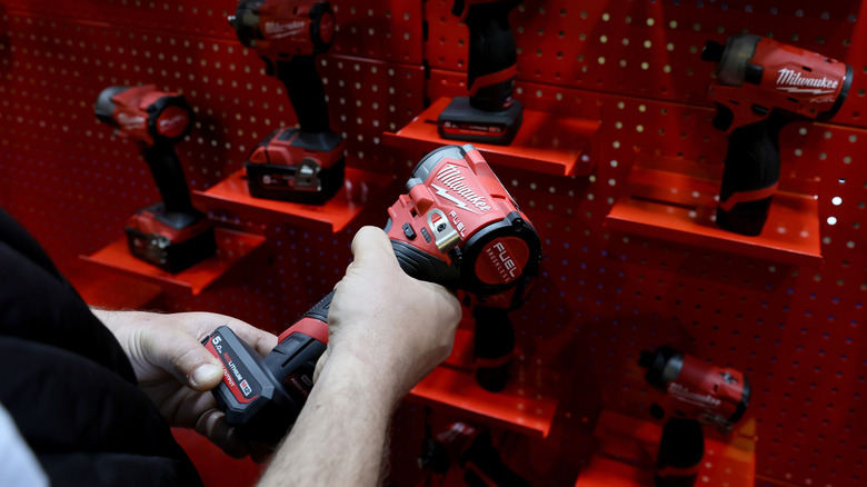 A person holding a Milwaukee tool in front of a brand display in a store