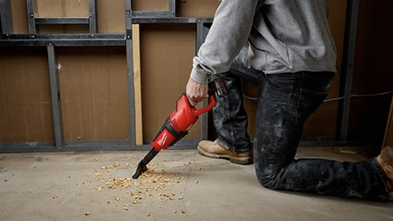 A man vacuuming up sawdust on a workshop floor with a red Milwaukee vacuum