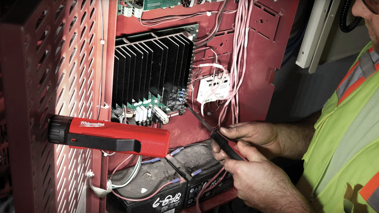 A man working on an electrical panel using a magnetic flood light mounted to the inside of the panel door