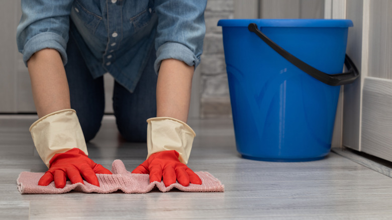 person cleaning floor with bucket and rag