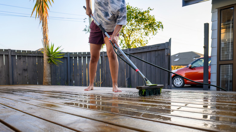 Man cleaning his wooden deck with a large brush and a water sprayer