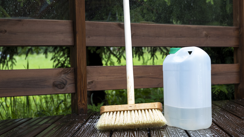 A brush with a bottle of a chemical solution on a wood deck