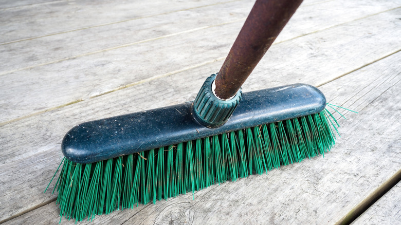 A stiff brush with green bristles on a wood deck