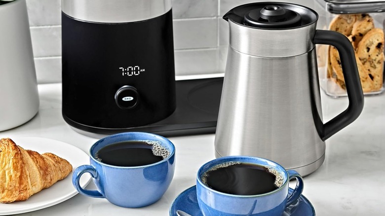 OXO coffee maker on a counter next to two cups of coffee