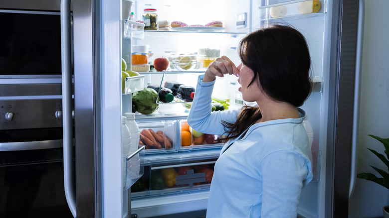 Woman pinching her nose against the rotten smell coming from an open fridge