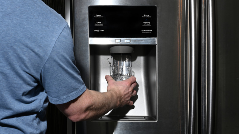 Male filling a glass of water via the water dispenser on a fridge