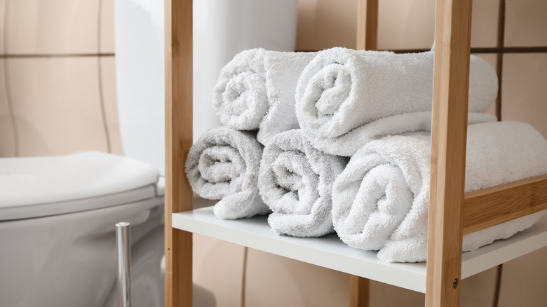 five white towels rolled up on a shelf near a toilet