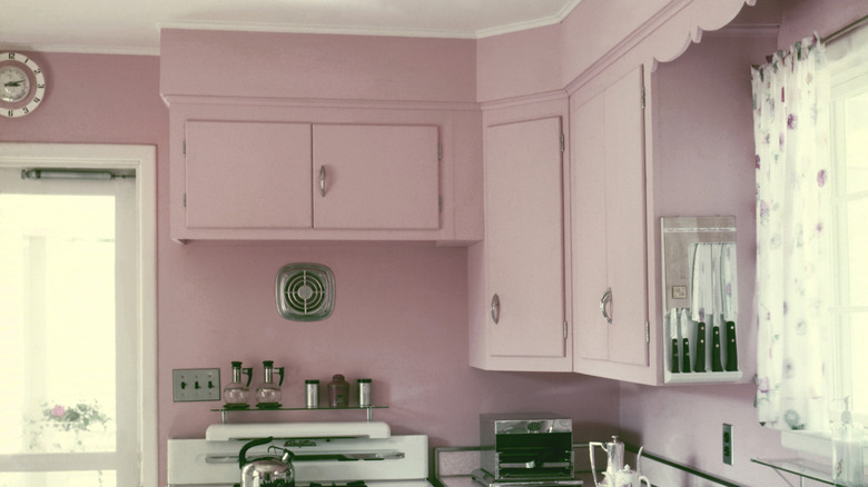 A vintage kitchen has pink walls and dainty details