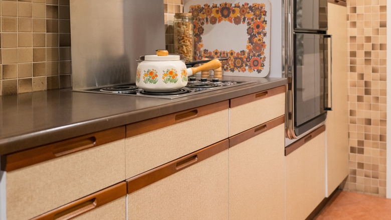 A 1950s kitchen shows clean lined white and wood cabinets and a built-in stove