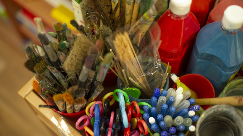 An organizer filled to the brim with paint brushes, paint, scissors, cups, and pens