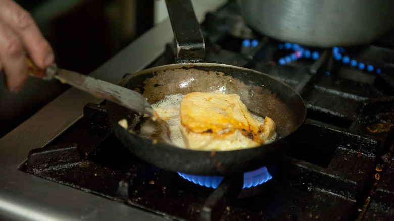 Person frying fish in a pan on a gas stove