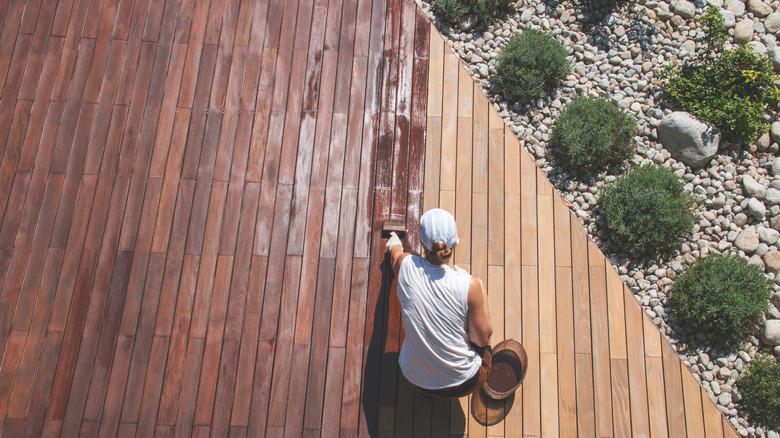 man applying stain on wooden deck