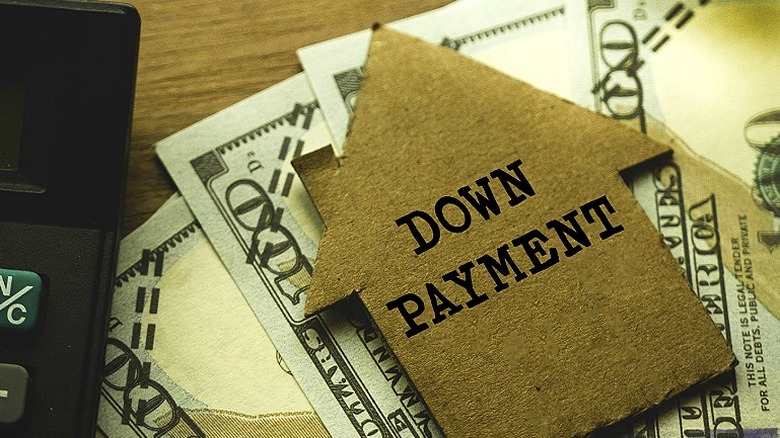 A piece of house-shaped cardboard with the words down payment on it placed over dollar bills