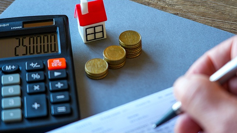 Close-up of a person's hand calculating something related to a home using a calculator and pen and paper
