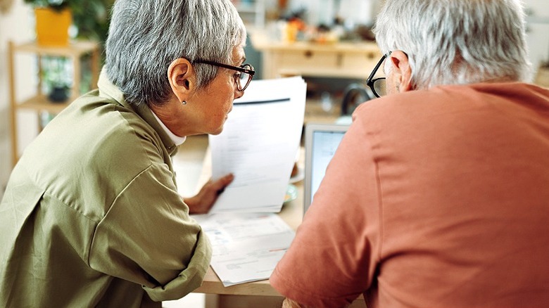 A couple is comparing documents and discussing them at a table and laptop