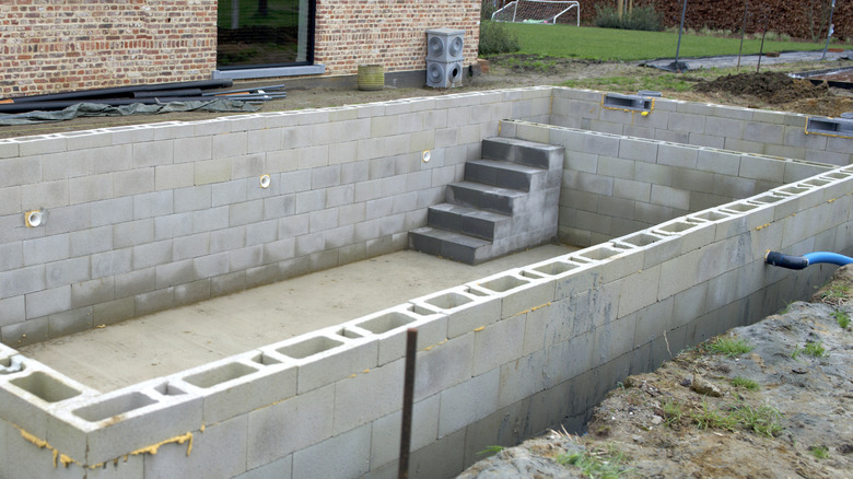 A person making a pool frame out of concrete blocks with stairs and holes for water filtration already
