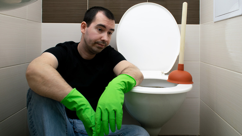 Man sitting by clogged toilet
