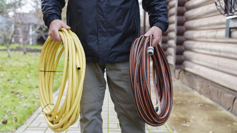 Man holding a rolled garden hose in each hand