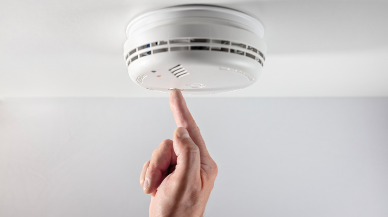 Finger pushing a button on a smoke alarm.
