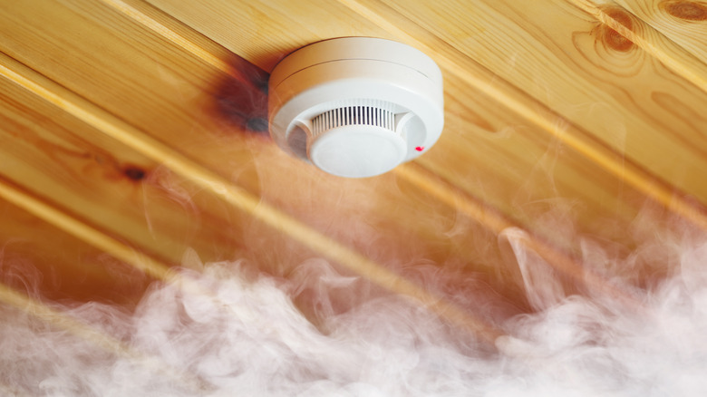 Smoke alarm with a red light on and smoke filling the room.