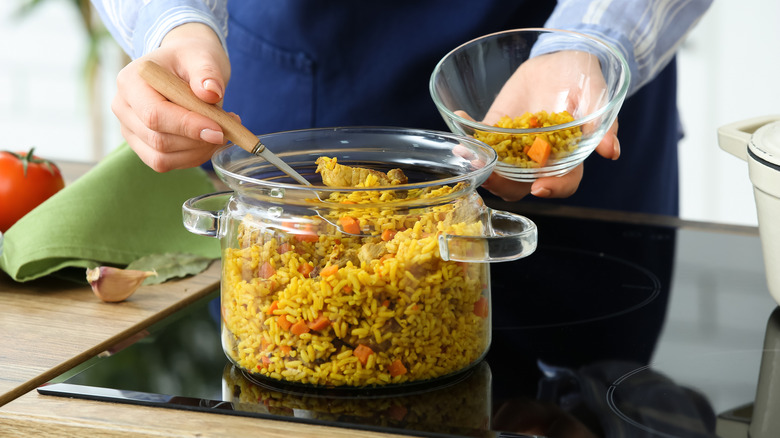 person dishing out cooked rice out of a glass pot on a glass cooktop