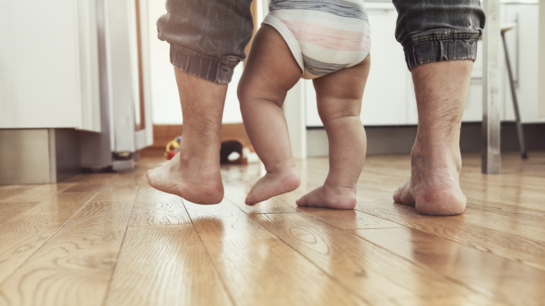 I piedi del bambino e del genitore sul pavimento di legno duro