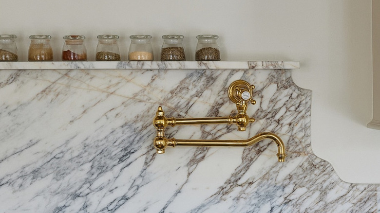 A brass faucet against a marble wall.