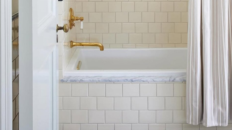 A white marble and tile bathroom with brass bath fixtures.