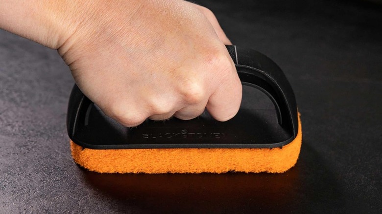 A person using a scouring pad to clean a Blackstone