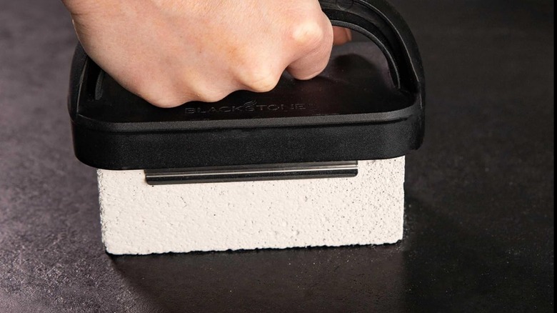 A person using a pumice stone to clean a Blackstone