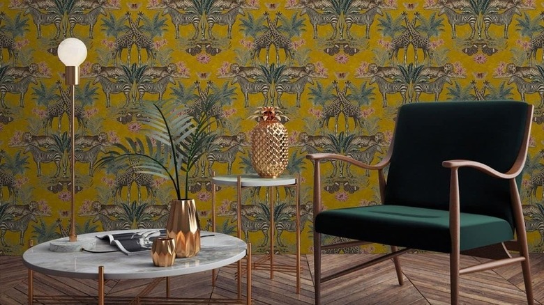 Tropical ochre wallpaper in a sitting room with a chair and a palm plant