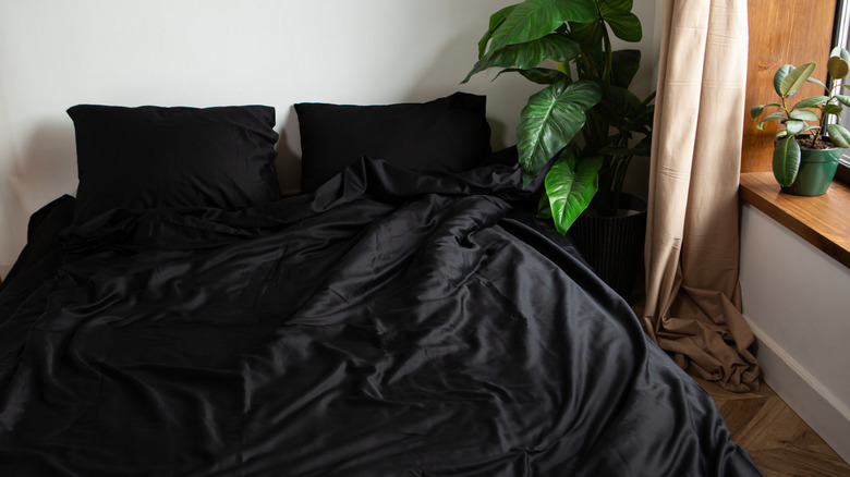 A bed with black sheets and plants