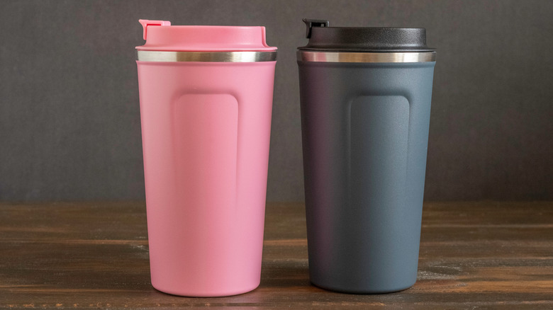 Two travel mugs sit on a kitchen counter.
