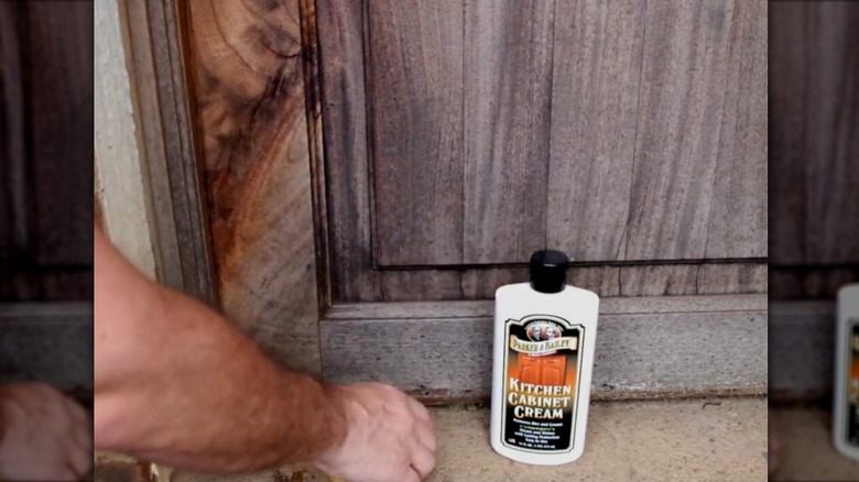 Someone wiping a dark wood cabinet with a yellow cloth.