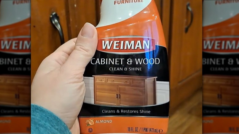 A man wearing a yellow glove wiping a wood cabinet.