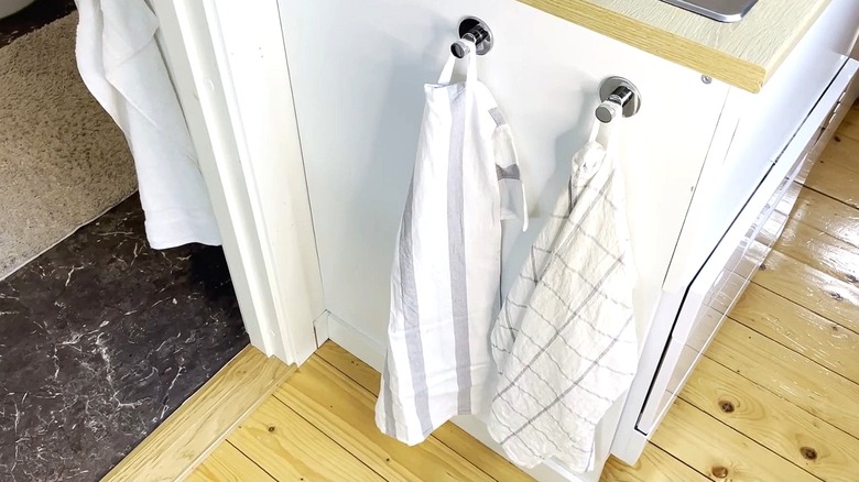 Two tea towels hang from hooks on the side of a kitchen cabinet.