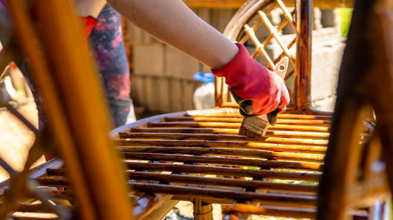 Close-up of a person applying oil or stain to wooden garden furniture